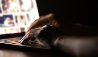 Hands typing on a laptop against a dark background illustrating menacing online safety in 2024