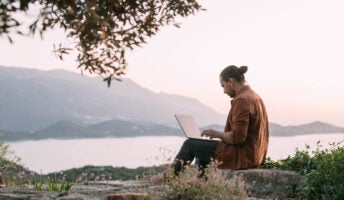 Man working remotely on laptop overlooking mountains and sea